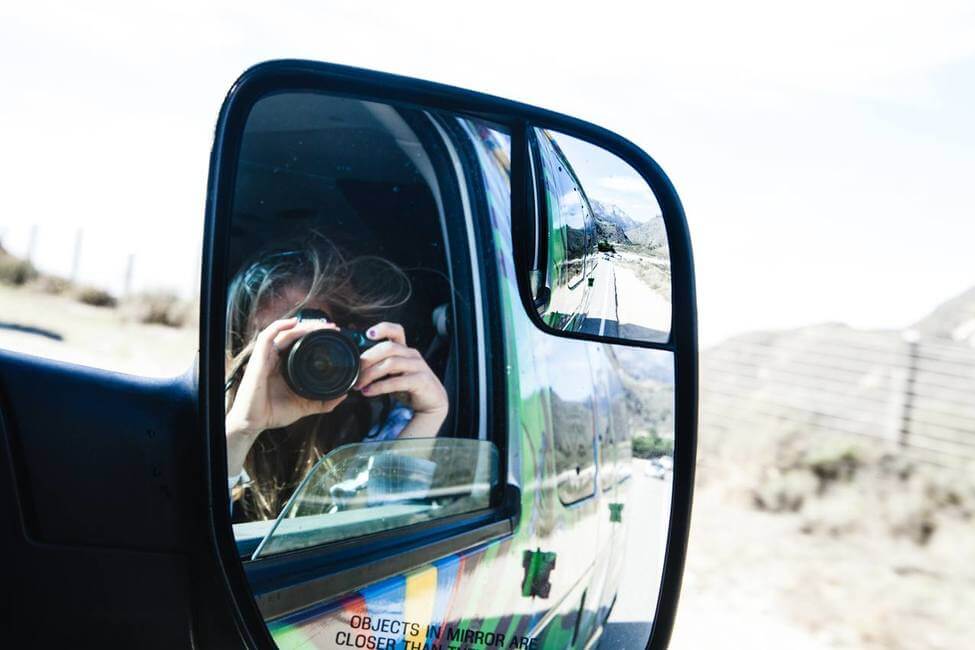 A woman taking a photo with her camera on a road trip with Escape Campervans