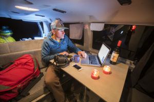 A man on his laptop sitting at the table in a campervan at night