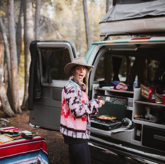Woman preparing breakfast in back of campervan.