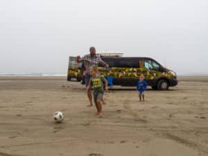Family playing on a beach next to a campervan