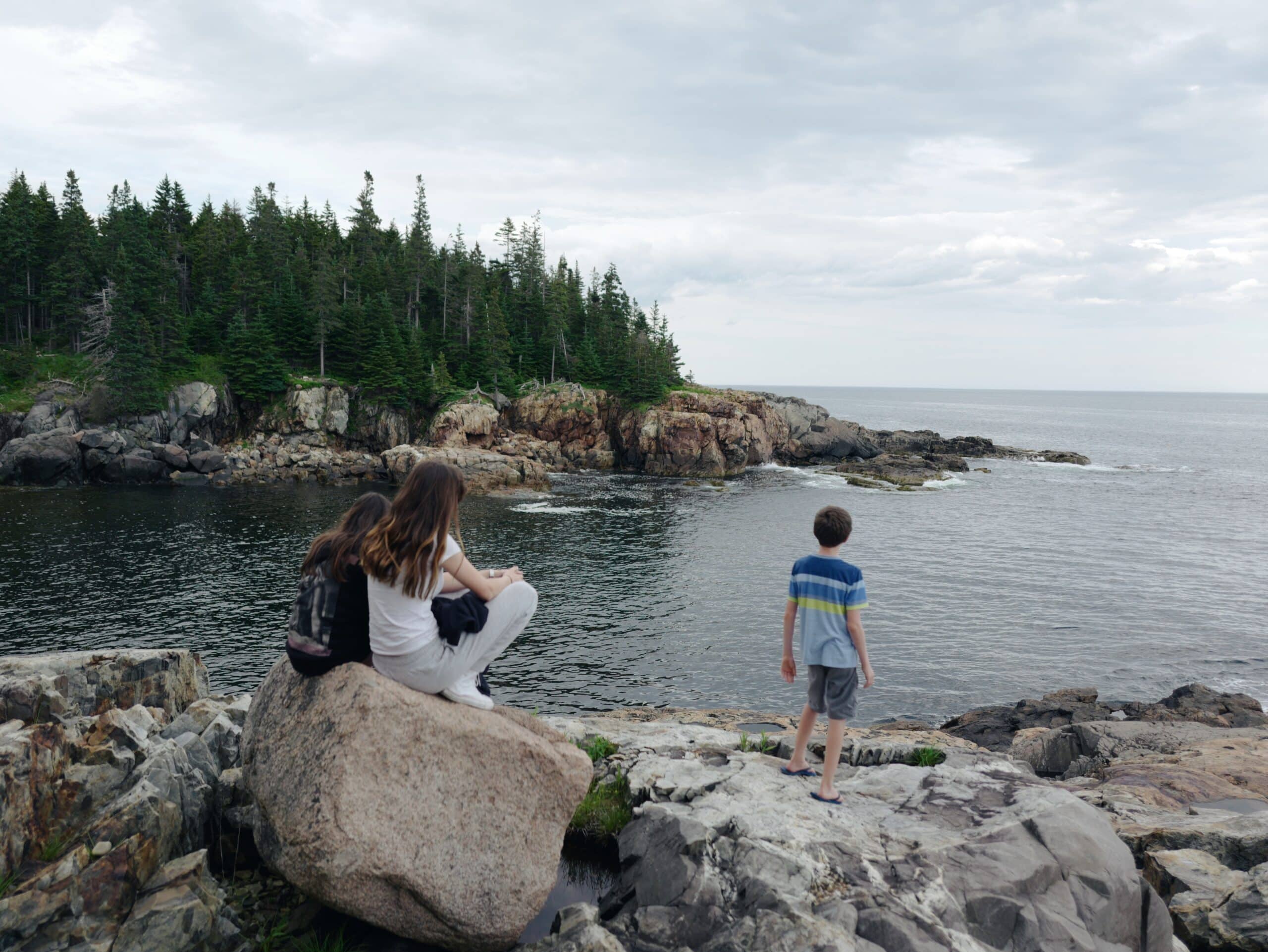 Family sitting on the rocky coastline of New York on a camper van road trip.