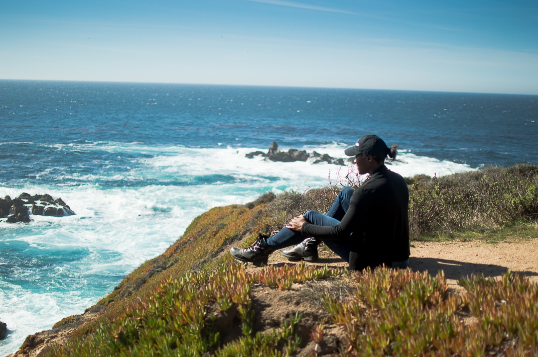 A woman sitting on the coast on a San Francisco to Big Sur road trip.