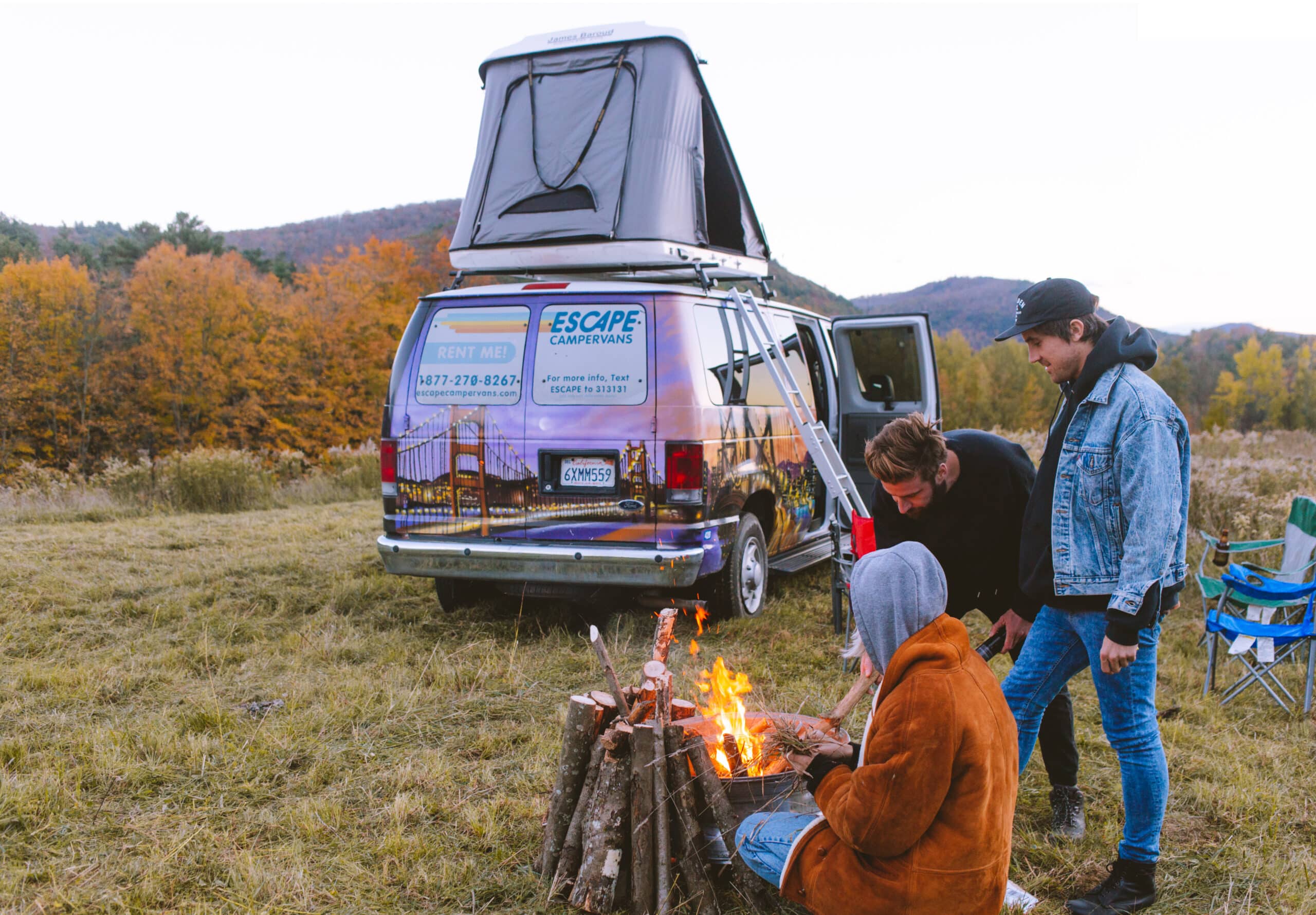 Friends sitting around a campfire sitting infront of an Escape Camper Van.