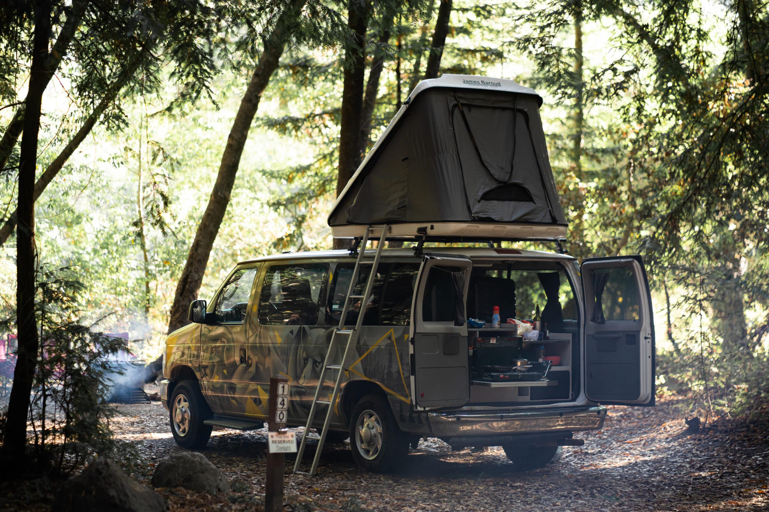 An Escape camper van with a rooftop tent set up to camp in the California woods.