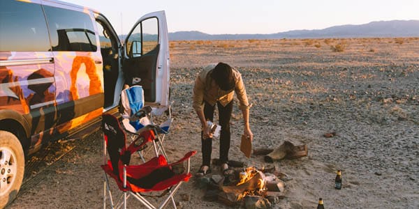 A person lighting a camp fire on a San Francisco road trip in an Escape Camper Van.